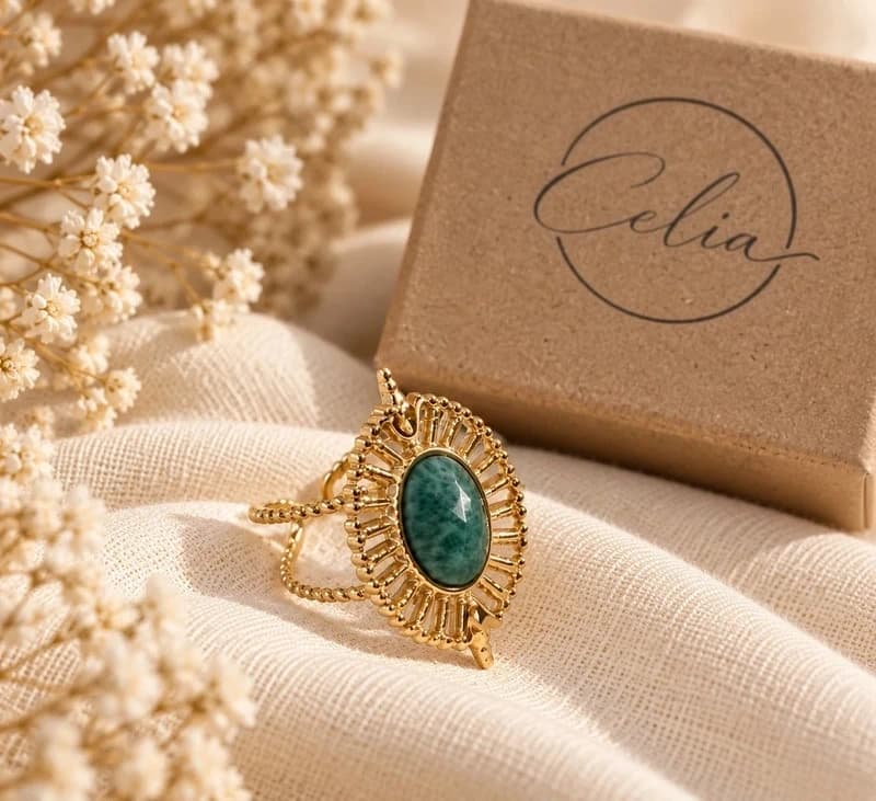 Anillo dorado con piedra verde sobre lino y packaging Celia